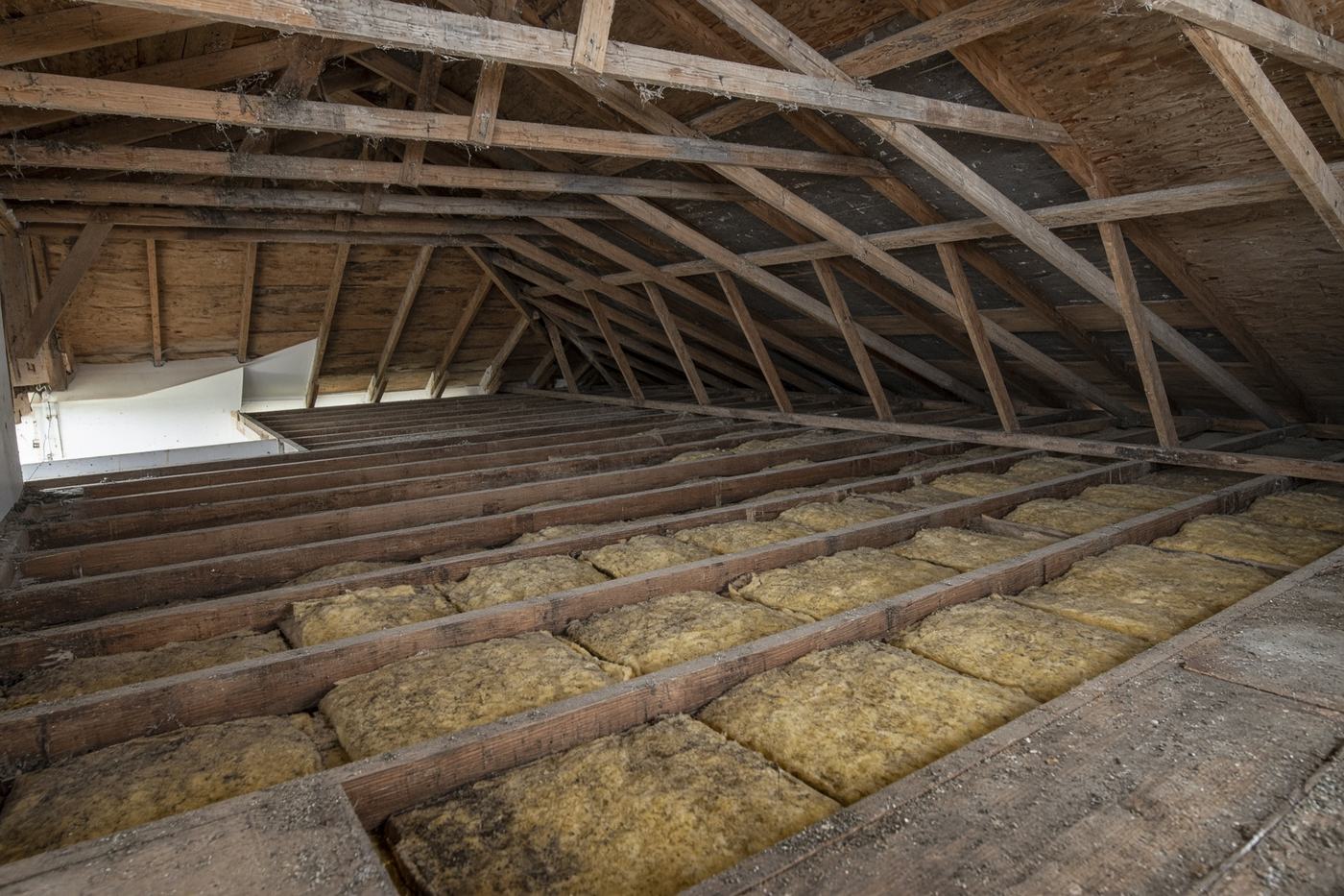 Thin yellow fiberglass batts with gaps between attic joists before a blown-in top-up